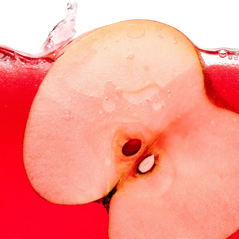Halved red apple splashing into red liquid